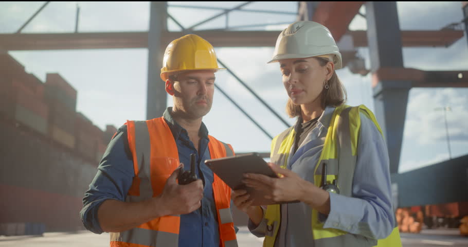 Male and Female Logistics Workers Use a Tablet and Radio to Manage Container Operations at a Port, Shipping Cranes and Cargo. Cranes Loading Commercial Containers. Shipment Dispatch Freigh Terminal
