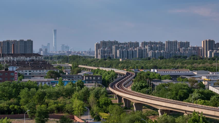 Elevated subway rail tracks curve through green urban landscape with modern apartment buildings and Beijing CBD skyline in background under blue sky