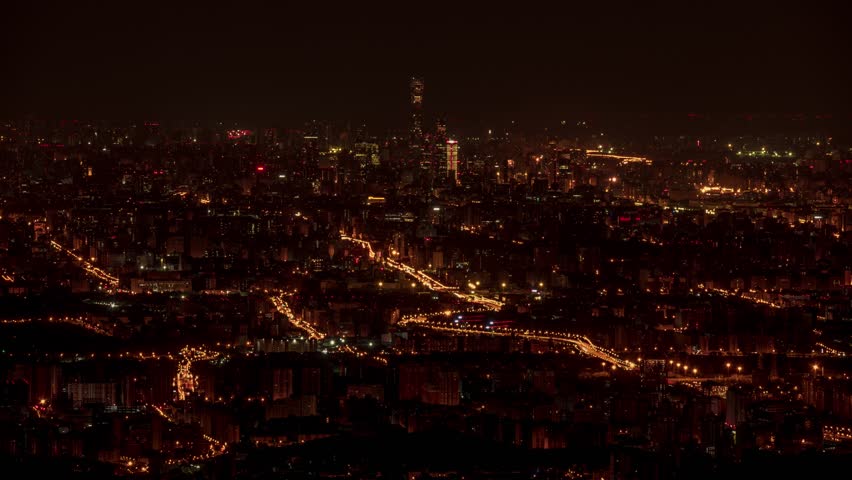 Stunning aerial night view of Beijing cityscape with illuminated buildings, highways, and urban infrastructure creating golden light trails across the metropolitan area.