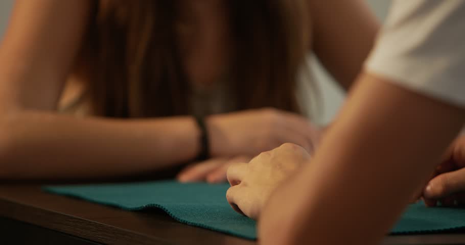 Two siblings, a boy and a girl, teenagers playing cards at home. Shot of hands cutting the deck.