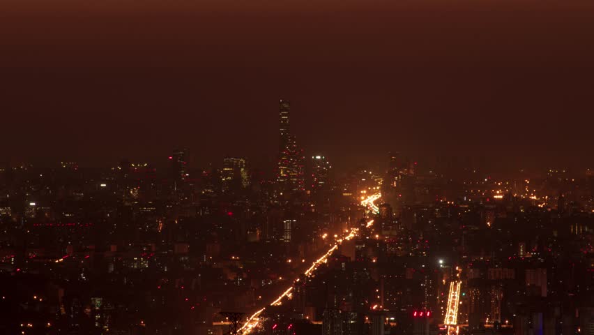 Time lapse view of Beijing city skyline at night with illuminated buildings and traffic trails creating a warm golden glow across the urban landscape in China.