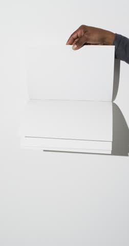 Vertical video of hand of african american man with book with white blank pages on white background. Book, literature, paper, writing, texture and materials concept, copy space.