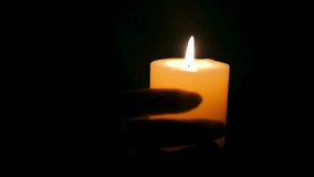 A person's hand holds a single burning candle in complete darkness. The warm flame flickers, illuminating the wax against a pitch black background. - Powered by Shutterstock - Get 15% off with code: PIKWIZARD15