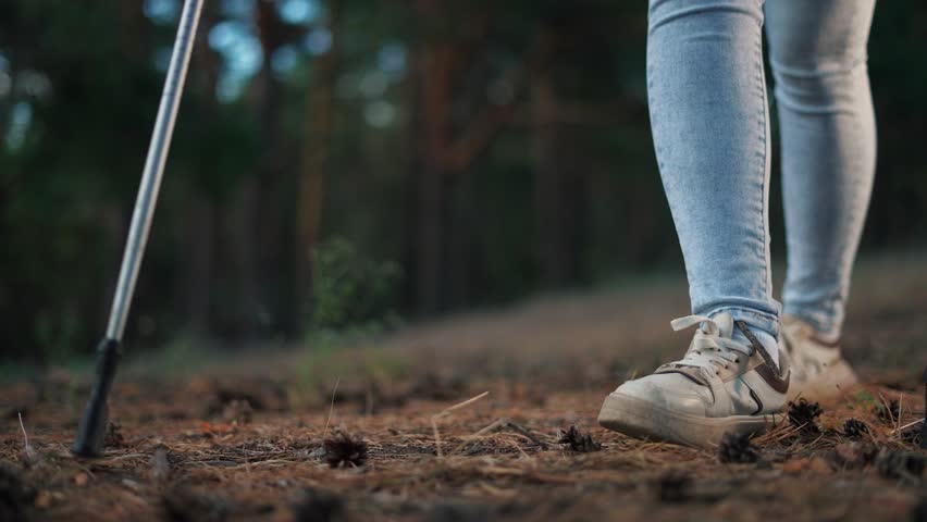 A woman walks on her legs through a forest in the nordic walking. Tourism travel adventure concept. Girl walks through a forest with sticks. Girl walks on sticks lifestyle her legs through a forest.