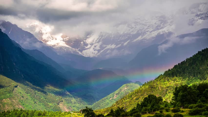 Time lapse view of rainbow over Namcha Barwa peak in Himalayan mountains with dramatic clouds and lush green valleys below