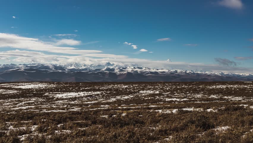 Time lapse view of snow-covered Gongga mountain range in Ganzi Tibetan Autonomous Prefecture, Sichuan, China under dramatic blue sky with white clouds