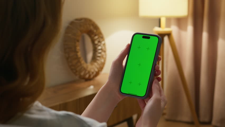 Woman use digital tech cell phone with green screen mock up. Hand tap press iphone web site, open app. Girl hold mobile closeup. Turn on page. Cozy home background. Click online game copy space.