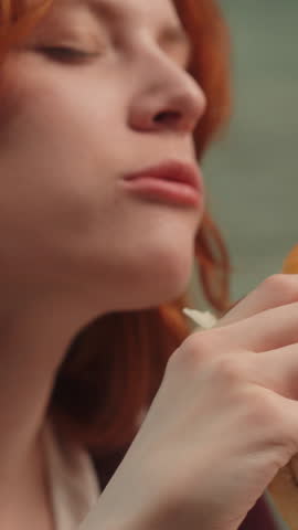 Satisfied Caucasian woman female girl eating junk fast food bite chewing tasty burger hamburger cheeseburger at home eat unhealthy meal diet nutrition disorder cheat meal overeating calories obesity