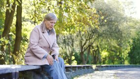 Elderly female with gray hair suffers from painful severe knee joint pain sitting on bench on street in urban city park. Upset woman massages leg muscles, could not walk, illness, cramps or rheumatism - Powered by Shutterstock - Get 15% off with code: PIKWIZARD15