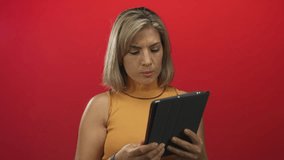 Blonde young woman holding tablet, hand to forehead and raised palm while reading screen in studio with red wall; surprise. - Powered by Shutterstock - Get 15% off with code: PIKWIZARD15
