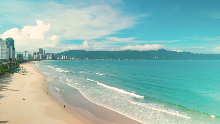 Da nang city skyline rises along my khe beach. Waves washing onto the sandy shore. Creating a dynamic seascape with mountains framing the horizon. Embodying tropical travel and summer holiday concepts