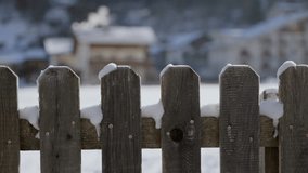 Rustic wooden fence with snow by a chalet rural cabin with chimney in background. Smoke coming out during cold winter season outdoors in European Alps. Sunny day in countryside or ski resort. Close up - Powered by Shutterstock - Get 15% off with code: PIKWIZARD15