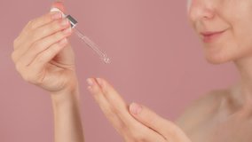 Pipette of serum in the hands of a young woman with radiant skin. Macro close-up drops of serum dripped from the dropper. Beauty routine on a pink background. Slow motion. Cosmetic concept ads - Powered by Shutterstock - Get 15% off with code: PIKWIZARD15