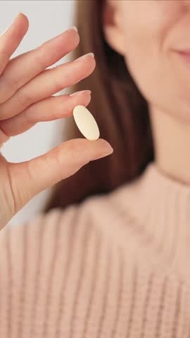 Vertical close-up of an unrecognizable woman holding a a vitamin pill, smiling before taking the pill. Concept of daily health and wellness routine.