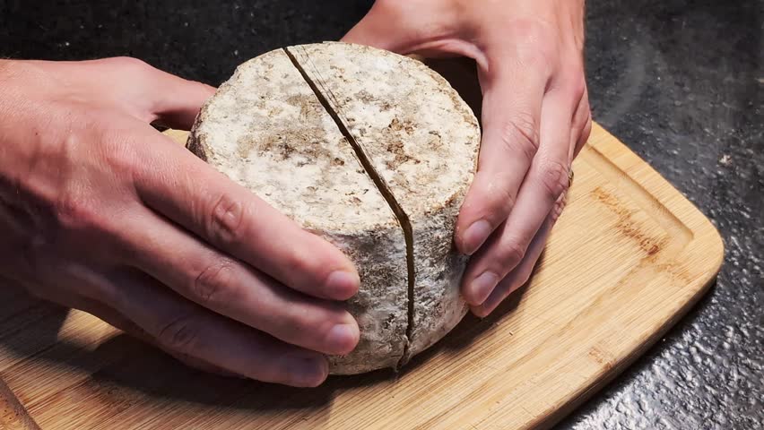 Man's hand open a wheel of Tomme cheese, cut in half. Local fresh food concept.