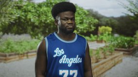 Man with eyes closed standing in a blue basketball jersey in a city park near raised planters and greenery; contemplation. - Powered by Shutterstock - Get 15% off with code: PIKWIZARD15