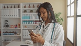 Hispanic female doctor using phone in a modern clinic, wearing stethoscope, surrounded by medical equipment and documents, showing professional work environment indoors. - Powered by Shutterstock - Get 15% off with code: PIKWIZARD15