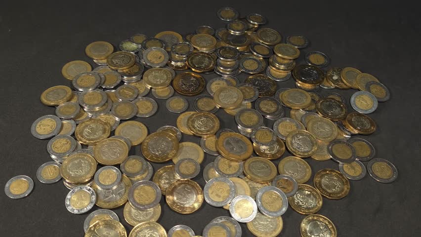 Wealth accumulation: Rolls of money falling on a bed of coins, investing and saving in Mexican pesos