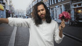 Man in white shirt extends arm pointing while holding pink bouquet on street, staring at camera; romance longing. - Powered by Shutterstock - Get 15% off with code: PIKWIZARD15