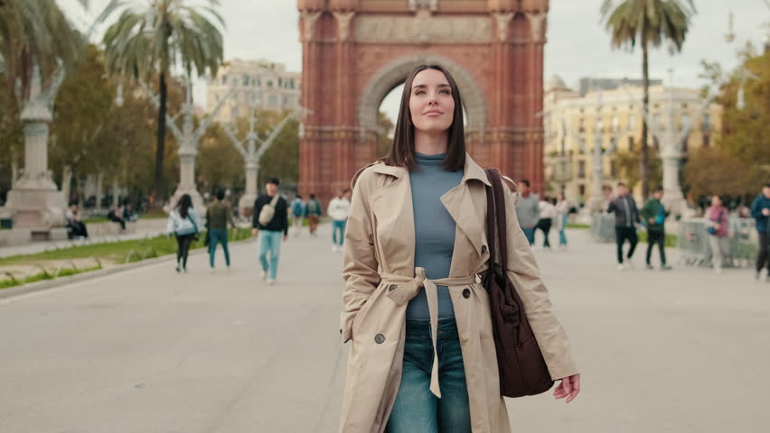Young woman walks towards Arc de Triomf in Barcelona, Spain. She's enjoying a beautiful day in the city.