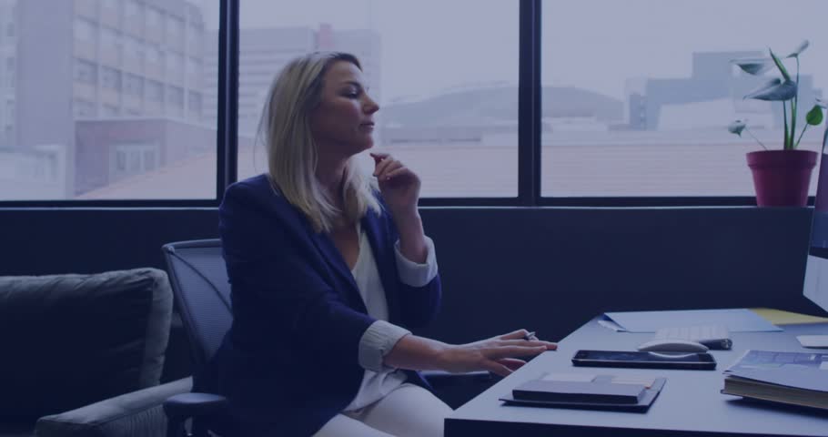 Mature woman at business desk, noticing play icon near hand tapping midair controls managing popups. Professional, technology, modern, corporate, productivity, digital, interior