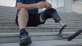 Male amputee athlete with running blade prosthetic resting on outdoor stairs after jogging, close up shot. Disability, sport, and recreation concept. - Powered by Shutterstock - Get 15% off with code: PIKWIZARD15