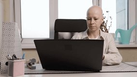 Young woman with alopecia sitting at desk and browsing laptop, cancer awareness and workplace inclusivity representation, home office productivity scene - Powered by Shutterstock - Get 15% off with code: PIKWIZARD15