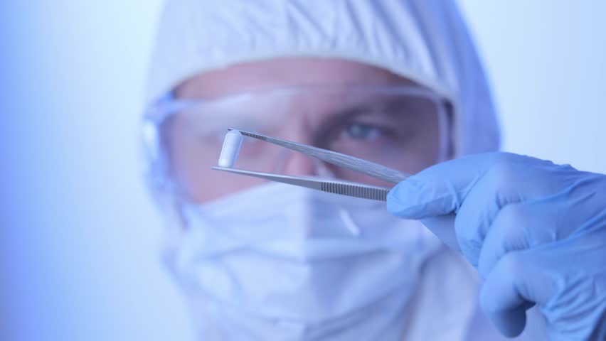 Man worker inspects pill capsules for control medicine quality in pharmaceutical facility, blue light background.