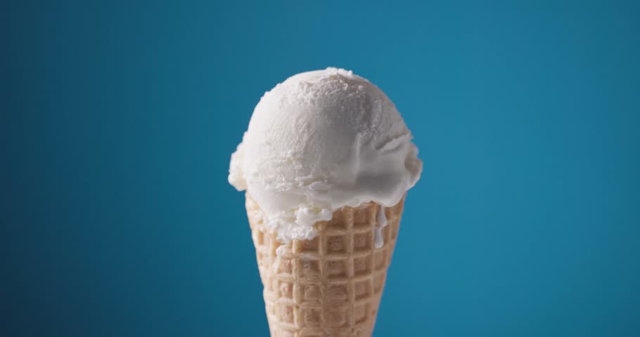 Melted chocolate sauce flowing over a scoop of vanilla ice cream in a waffle cone, set against a blue background