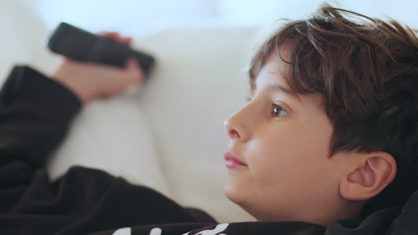 Close-up of an 8-year-old boy sitting on the couch, completely focused on the television, holding a remote as his mouth hangs open in pure fascination and wonder.	