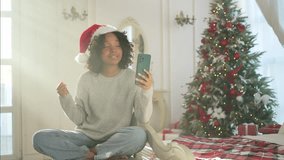 Merry Christmas. African woman in Santa hat having video chat in smartphone. Blogger in festive mood recording video in social network. Girl having video call with friends family celebrating Christmas - Powered by Shutterstock - Get 15% off with code: PIKWIZARD15