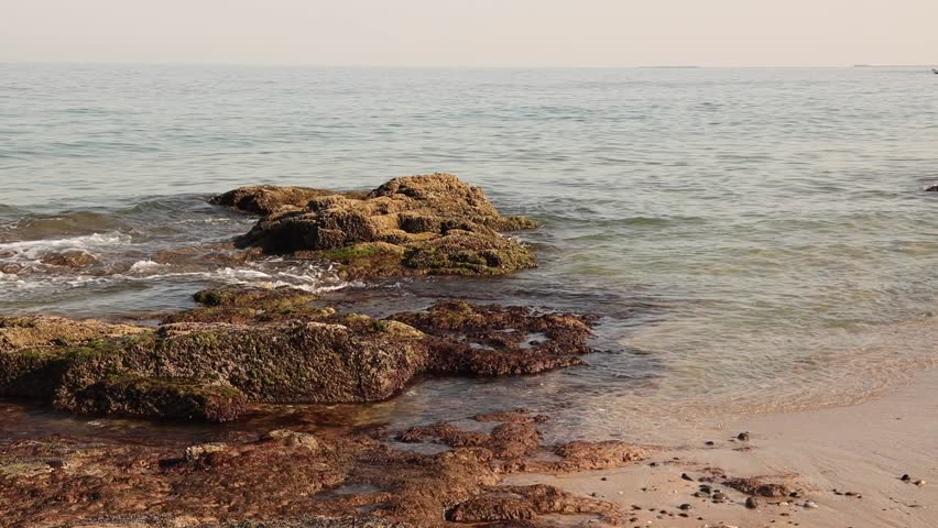 Rocks in a calm sea. A motorboat passes in the background.
