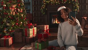 Merry Christmas. African woman in Santa hat having video chat in smartphone. Blogger in festive mood recording video in social network. Girl having video call with friends family celebrating Christmas - Powered by Shutterstock - Get 15% off with code: PIKWIZARD15