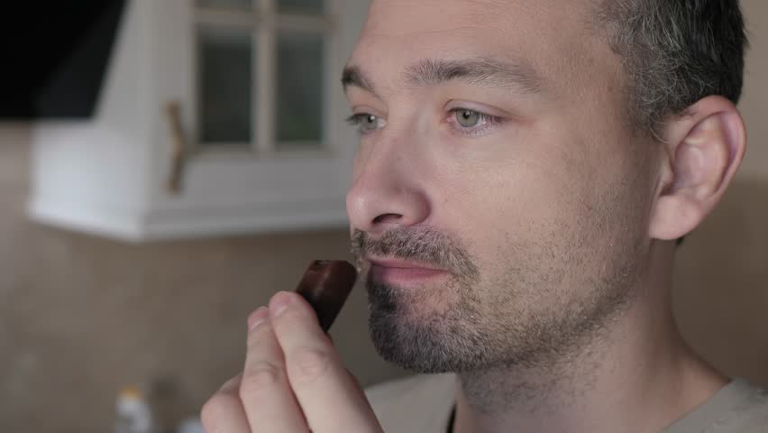 Man is enjoying decadent dark chocolate treat, close up, beautifully captured through closeup shots that emphasize his facial expressions and the delectable chocolate dessert he holds in his hand