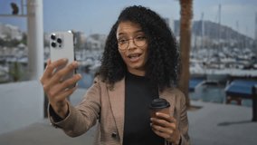 Young woman in check blazer holds smartphone and coffee cup at port with marina view; connection joy. - Powered by Shutterstock - Get 15% off with code: PIKWIZARD15