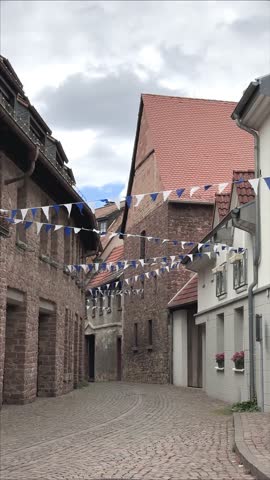 A quiet cobblestone street in a German old town with rustic buildings and festive blue and white flags hanging above.