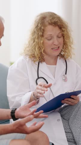 Professional female doctor explaining diagnosis to senior male patient during home visit. Vertical footage