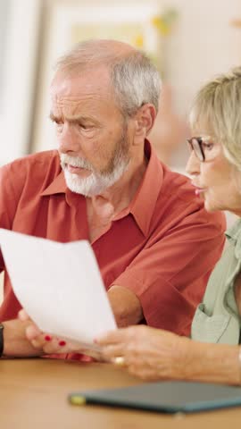 Retired couple nervously reviewing financial documents at home, displaying growing anxiety while discussing potential challenges affecting their future. Vertical footage