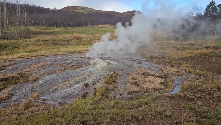 Steam billows from the bubbling geothermal vents at the Geyser Geothermal Area in Iceland’s Haukadalur Valley. The landscape features mineral-rich soil, hot springs, and distant rolling hills under a 