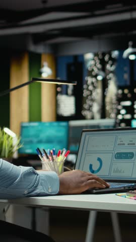 Vertical Video Black advisor researching market data and building strategy for business targets, using spreadsheets on laptop for proofreading. Late night overtime for a multinational company. Camera