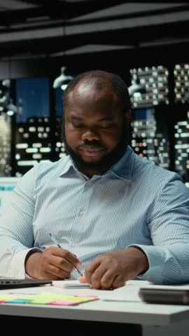 Vertical Video African american strategist ripping a paper after writing the wrong idea, restarting work in rage and crumpling the page sheet. Discontent man does a typo mistake while transcribing