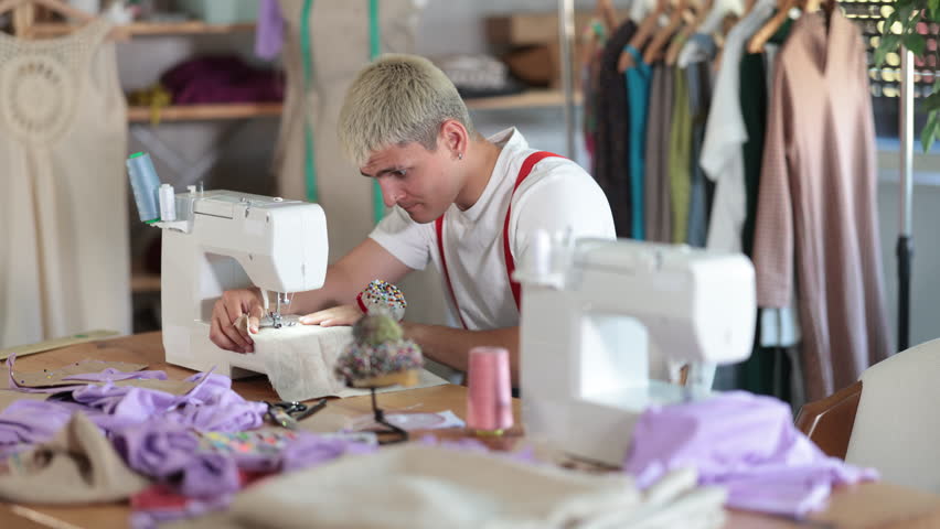 Young man tailor sews clothes on a sewing machine in the workshop. Fashion designer is working on the creation of a clothing collection. High quality 4k footage
