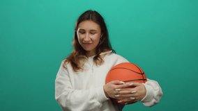 Woman smiling and holding basketball against vibrant green background, youthful energy highlighting casual style and playful nature in a simple isolated setting. - Powered by Shutterstock - Get 15% off with code: PIKWIZARD15