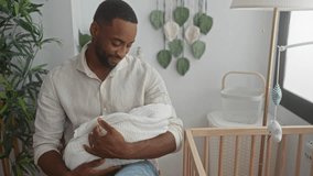 Man cradling swaddled baby with visible hands in nursery room near crib while seated and looking down; fatherhood tenderness. - Powered by Shutterstock - Get 15% off with code: PIKWIZARD15