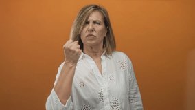 Caucasian woman clenching fist and shouting with open mouth in orange studio wearing a white blouse; anger. - Powered by Shutterstock - Get 15% off with code: PIKWIZARD15