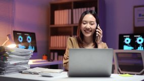 Young Asian businesswoman working late at night in office using laptop computer and talking on mobile phone while sitting at desk with stacks of paperwork - Powered by Shutterstock - Get 15% off with code: PIKWIZARD15