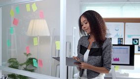 Young African American businesswoman carefully analyzing data on colorful sticky notes while methodically taking notes on clipboard inside sleek modern corporate workspace - Powered by Shutterstock - Get 15% off with code: PIKWIZARD15