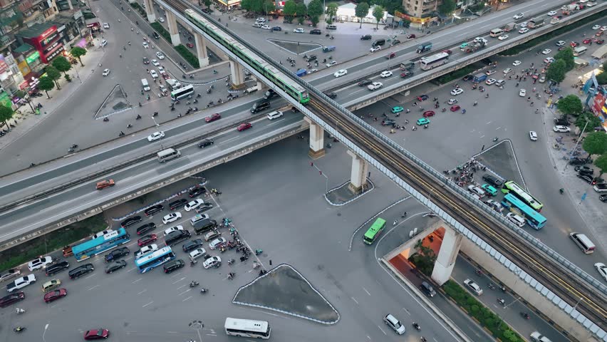 Aerial drone shot of Hanoi intersection with elevated metro line, buses, and cars at dusk.