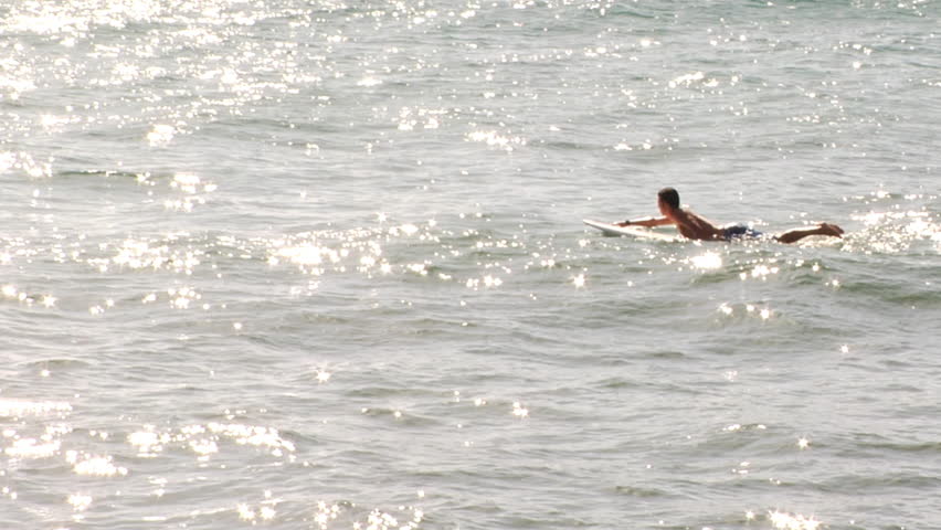 Surfer paddling out in the ocean under soft purple light of early dawn