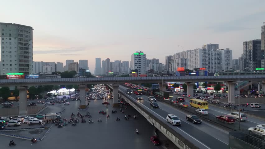 Evening scene of Hanoi city with metro overpass, busy traffic, and skyline buildings under fading light.